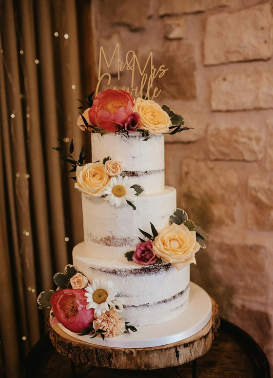 White three-tier cake with pink and orange flowers and cake topper